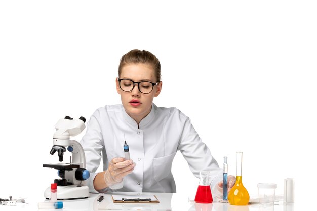 Front view female doctor in white medical suit with gloves holding injection on a white space