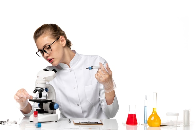 Front view female doctor in white medical suit with gloves using injection on a white desk