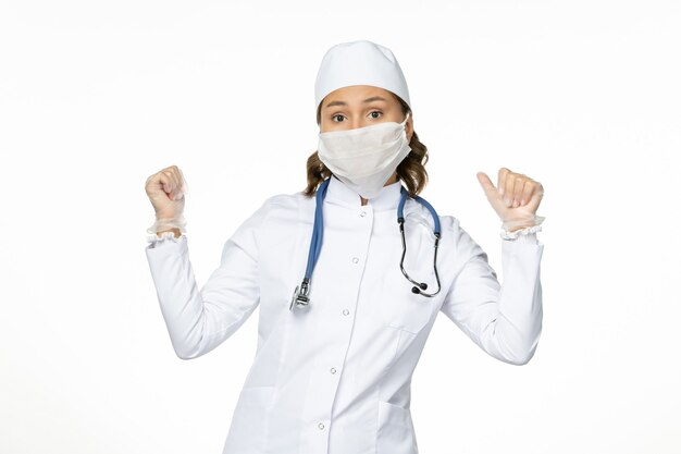 흰색 의료 복과 흰색 책상에 코로나 바이러스로 인한 마스크가있는 전면보기 여성 의사 바이러스 질병 격리 COVID