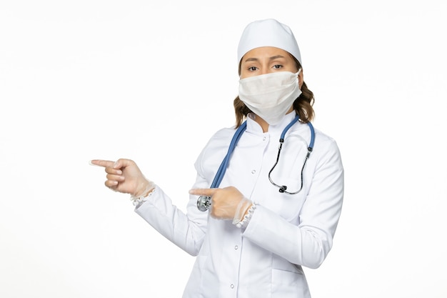 흰색 의료 복과 흰색 책상에 코로나 바이러스로 인해 마스크가있는 전면보기 여성 의사 바이러스 질병 전염병 covid