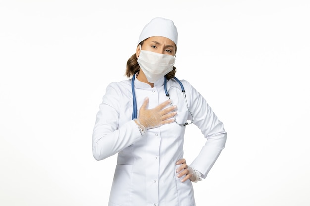 Front view female doctor in white medical suit and with mask due to coronavirus on white desk virus disease pandemic covid