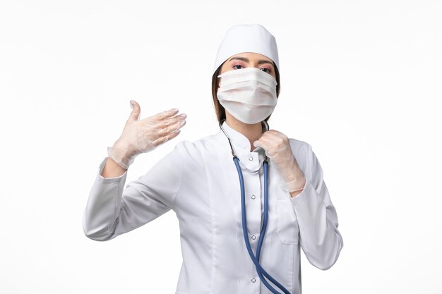白い壁の病気の病気のパンデミックウイルスcovidのコロナウイルスによるマスクと白い医療スーツの正面図の女性医師