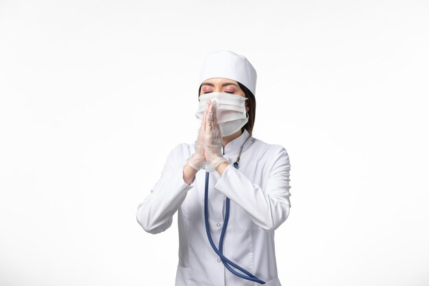 흰 벽에 코로나 바이러스로 인해 마스크가있는 흰색 의료 소송에서 전면보기 여성 의사 질병 의학 전염병 covid-