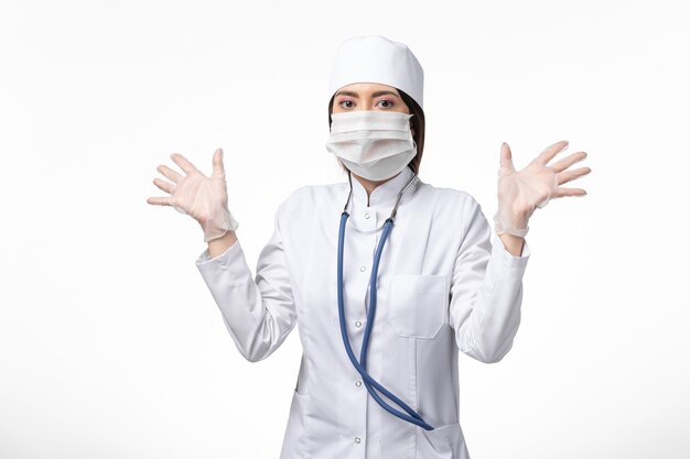 Front view female doctor in white medical suit with a mask due to coronavirus on the white wall disease medicine virus pandemic covid-