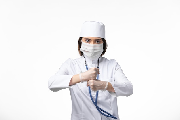 Front view female doctor in white medical suit with a mask due to coronavirus on white wall disease medicine virus pandemic