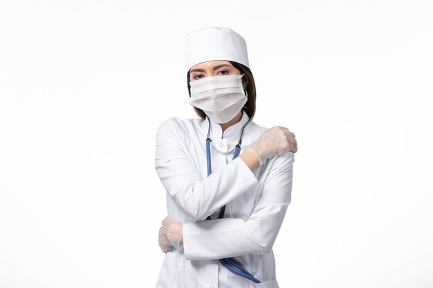 Front view female doctor in white medical suit with a mask due to coronavirus on white wall health disease pandemic covid-