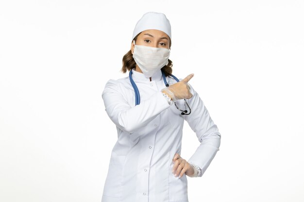 Вид спереди женщина-врач в белом медицинском костюме и с маской из-за коронавируса на белой стене пандемического вируса болезни covid