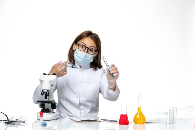 Front view female doctor in white medical suit with mask due to covid holding injection on white space