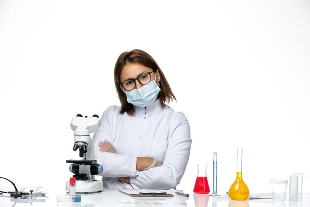 Front view female doctor in white medical suit with mask due to covid posing on light-white space