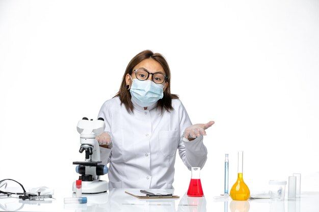 Front view female doctor in white medical suit with mask due to covid sitting on white space