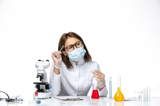 Front view female doctor in white medical suit with mask due to covid thinking on a white space