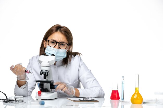 Front view female doctor in white medical suit with mask due to covid using microscope on white space