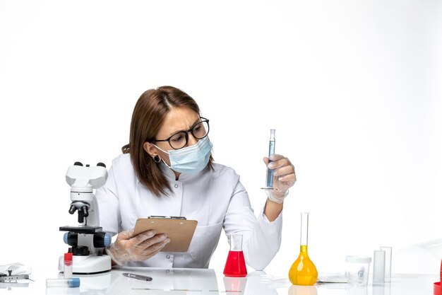 Front view female doctor in white medical suit with mask due to covid working on a white space