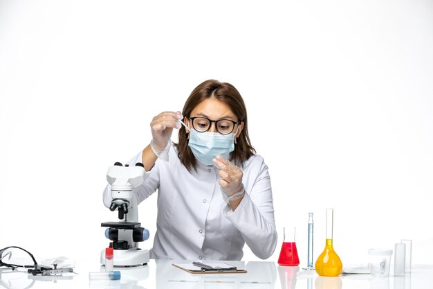 Front view female doctor in white medical suit with mask due to covid working on white space