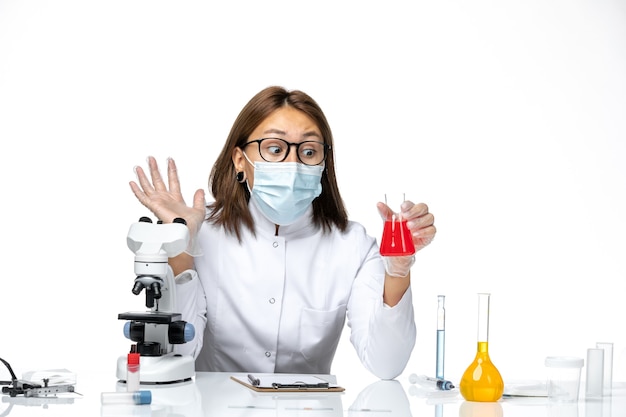 Front view female doctor in white medical suit with mask due to covid working with solutions on a white desk