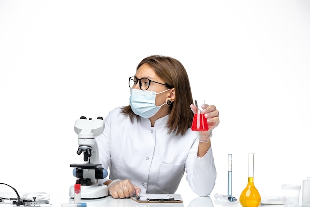 Вид спереди женщина-врач в белом медицинском костюме с маской из-за covid, работающего с растворами на белом пространстве