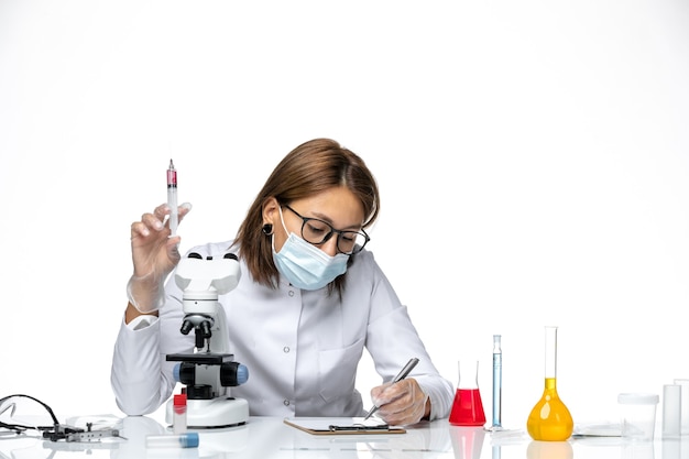 Front view female doctor in white medical suit with mask due to covid writing on light white space