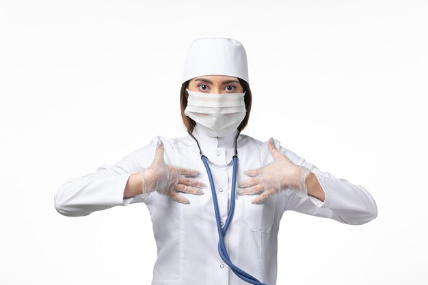 흰 벽에 전염병으로 인해 마스크가있는 흰색 의료 소송에서 전면보기 여성 의사 의학 대유행 바이러스 covid-
