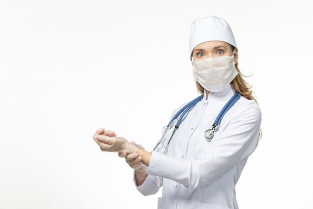 흰색 책상 질병 covid- pandemic 질병에 그녀의 맥박을 확인하는 코로나 바이러스로 인해 멸균 마스크가있는 흰색 의료 소송의 전면보기 여성 의사