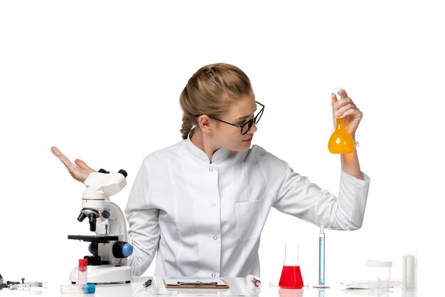 Front view female doctor in white medical suit working with solutions on a light-white space