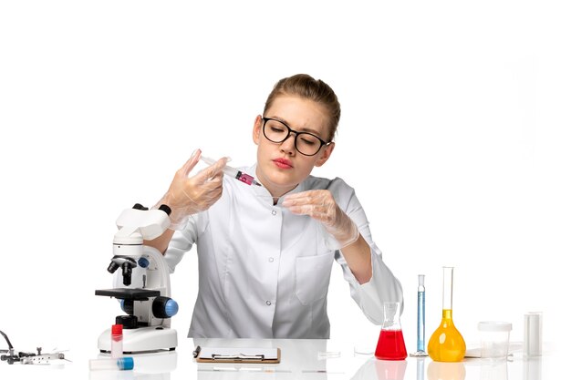 Front view female doctor in white medical suit working with solutions on the light white space