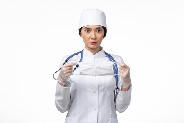 Вид спереди женщина-врач в белом стерильном медицинском костюме и держащая маску из-за болезни covid- на белой стене, болезни covid- пандемического вируса
