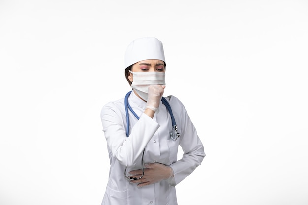 白い壁の病気ウイルスのパンデミック病で咳をしているため、白い無菌医療スーツを着てマスクを着用している正面図の女性医師