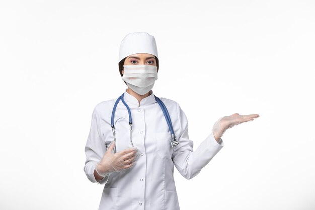 Front view female doctor in white sterile medical suit and wearing mask due to covid- on white wall virus covid- pandemic disease