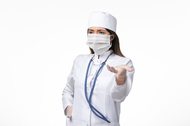 흰색 책상에 코로나 바이러스로 인한 마스크가있는 흰색 멸균 의료 복의 전면보기 여성 의사 covid- pandemic disease virus