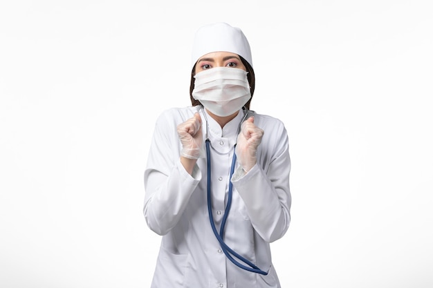 흰색 책상 질병 질병 전염병 covid- 바이러스에 코로나 바이러스로 인해 마스크가있는 흰색 멸균 의료 복의 전면보기 여성 의사