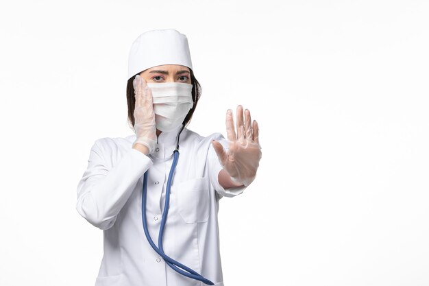 白い机の病気の病気のパンデミックウイルスのコロナウイルスによるマスク付きの白い無菌医療スーツの正面図の女性医師-