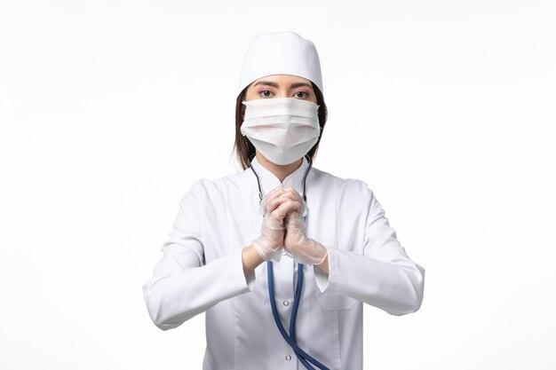 白い机の上のコロナウイルスによるマスク付きの白い無菌医療スーツの正面図の女性医師パンデミックコビッドウイルス