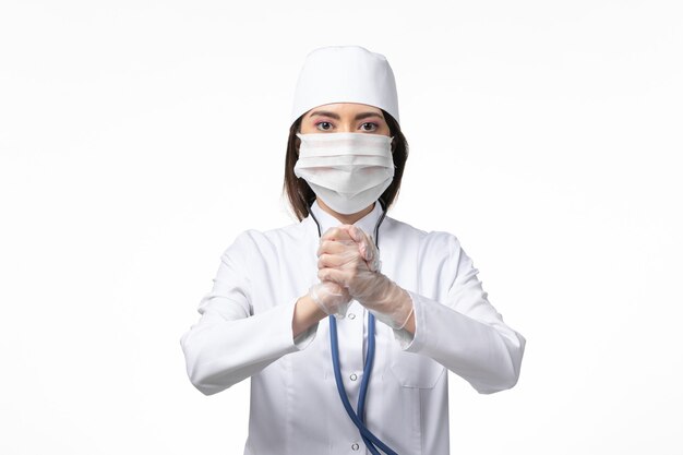 Front view female doctor in white sterile medical suit with mask due to coronavirus on white wall disease illness pandemic covid-