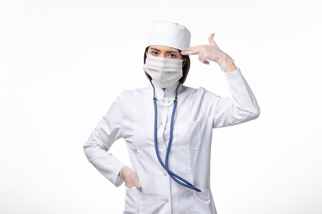 Front view female doctor in white sterile medical suit with mask due to coronavirus on white wall illness covid- pandemic virus