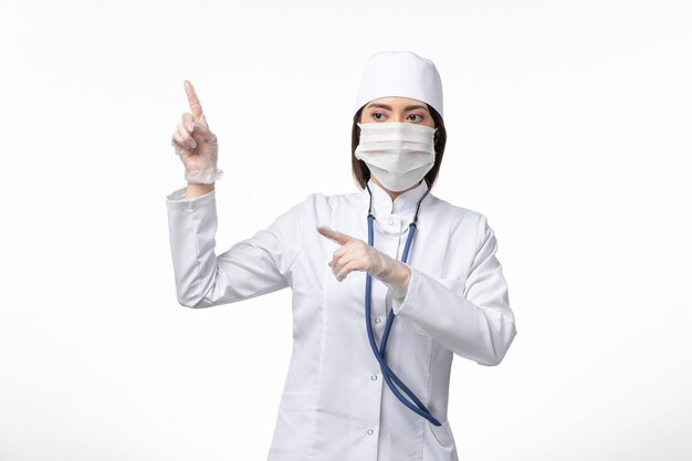 Вид спереди женщина-врач в белом стерильном медицинском костюме с маской из-за коронавируса на белой стене болезнь пандемическая болезнь covid-