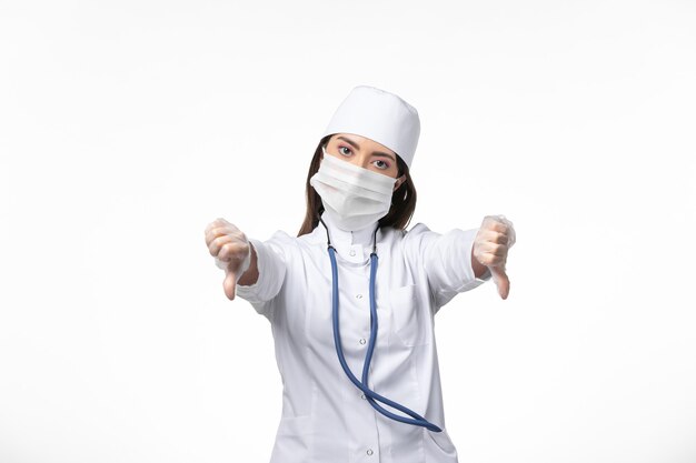 Front view female doctor in white sterile medical suit with mask due to covid- on light white wall illness covid- pandemic disease