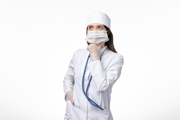 白い壁の病気の共同思考によるマスク付きの白い無菌医療スーツの正面図の女性医師