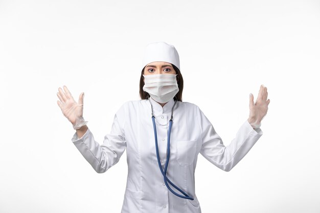 Front view female doctor in white sterile medical suit with mask due to covid- on white wall illness covid- pandemic