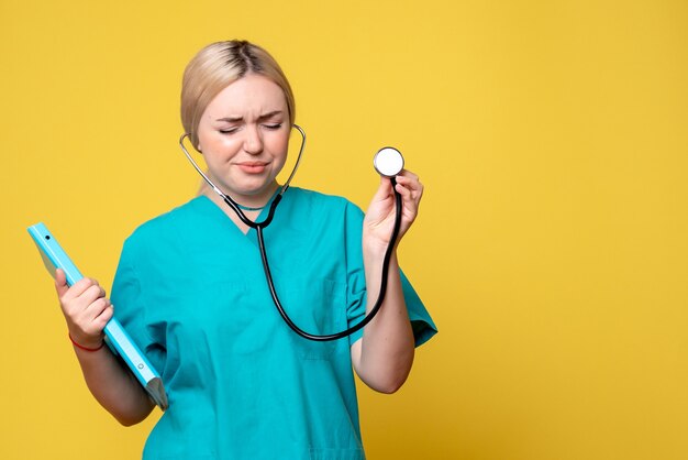 Front view of female doctor with analysis and stethoscope on the yellow wall