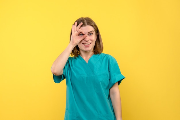 Вид спереди женщины-врача с возбужденным выражением лица на желтой стене