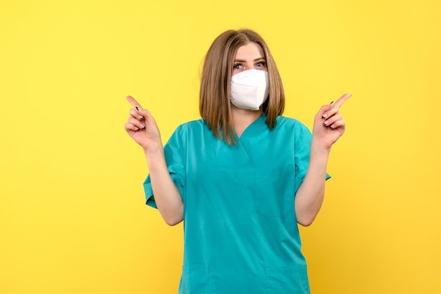 Front view of female doctor with mask on yellow wall