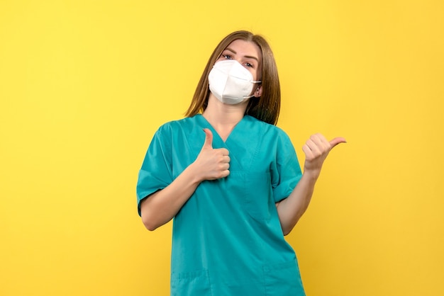 Front view of female doctor with mask on yellow wall