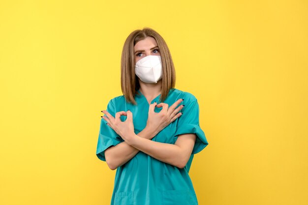 Front view of female doctor with mask on yellow wall