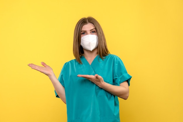 Front view of female doctor with protective mask on a yellow wall