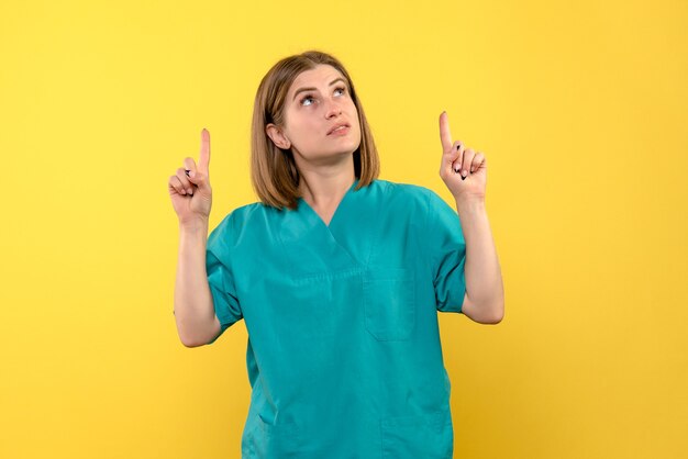 Front view of female doctor with raised fingers on yellow wall