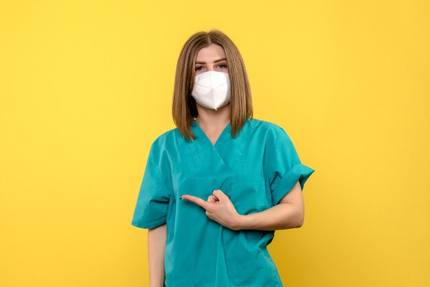 밝은 노란색 벽에 멸균 마스크가있는 여성 의사의 전면보기