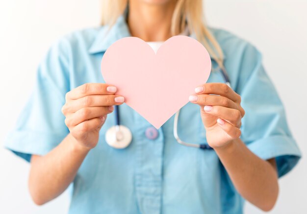 Вид спереди женщины-врача со стетоскопом, держащей бумажное сердце
