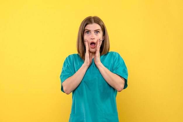 Front view of female doctor with surprised expression on yellow wall