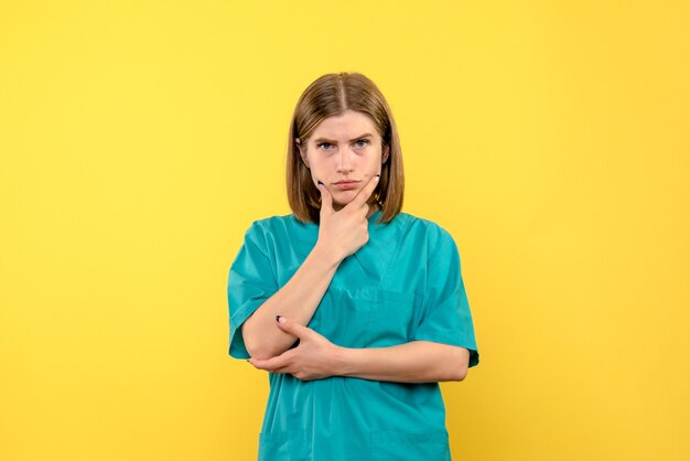 Front view of female doctor with thinking expression on yellow wall