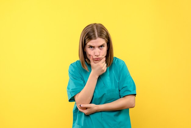 Front view of female doctor with thinking face on yellow wall
